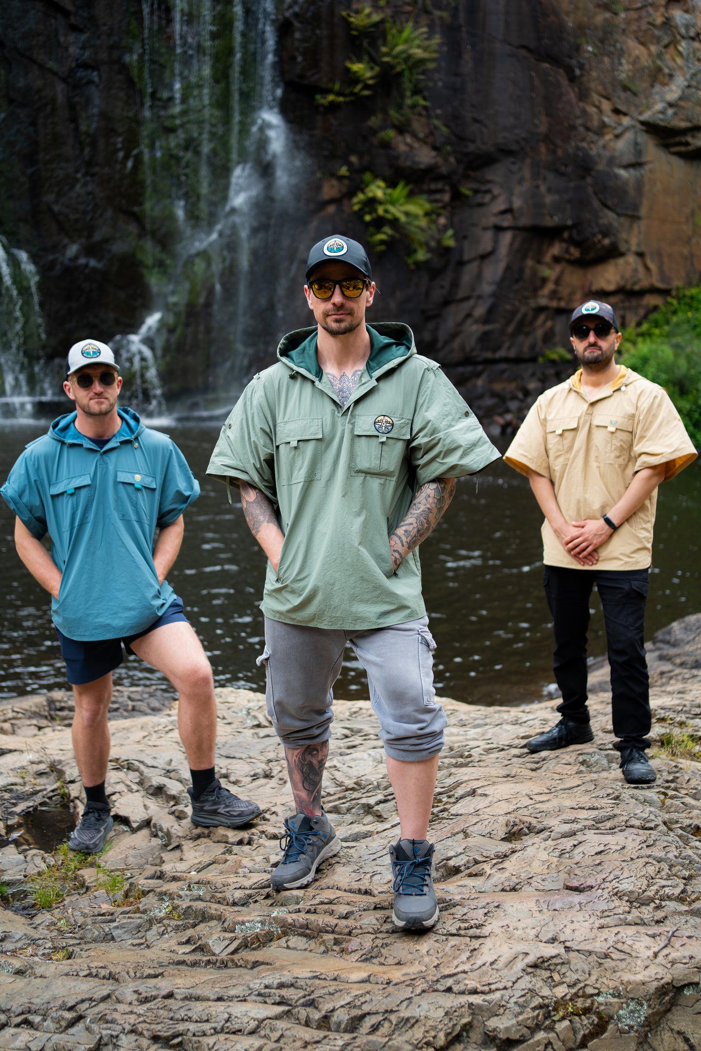 Three men standing on a rocky outcrop with a waterfall in the background