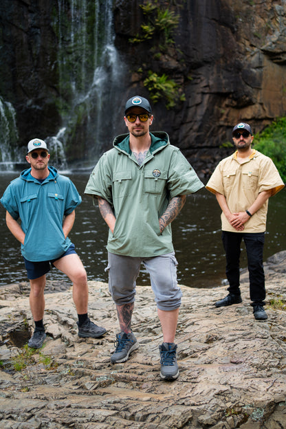 Three men standing on a rocky outcrop with a waterfall in the background